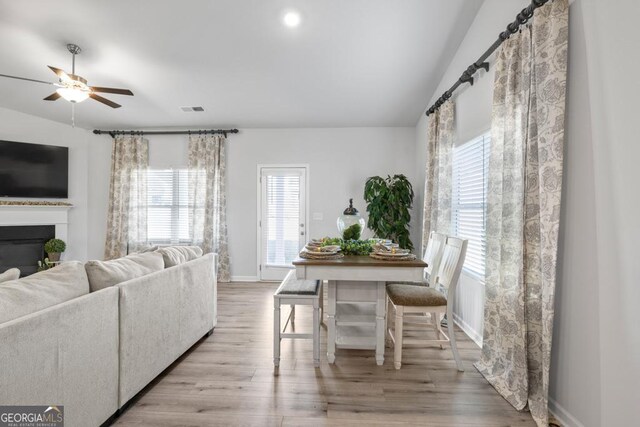 dining space featuring visible vents, a glass covered fireplace, ceiling fan, vaulted ceiling, and light wood-type flooring