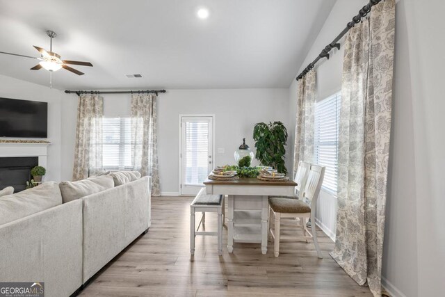 living room with a glass covered fireplace, vaulted ceiling, a ceiling fan, visible vents, and wood finished floors