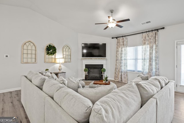 living area with lofted ceiling, a glass covered fireplace, ceiling fan, and light wood-style flooring