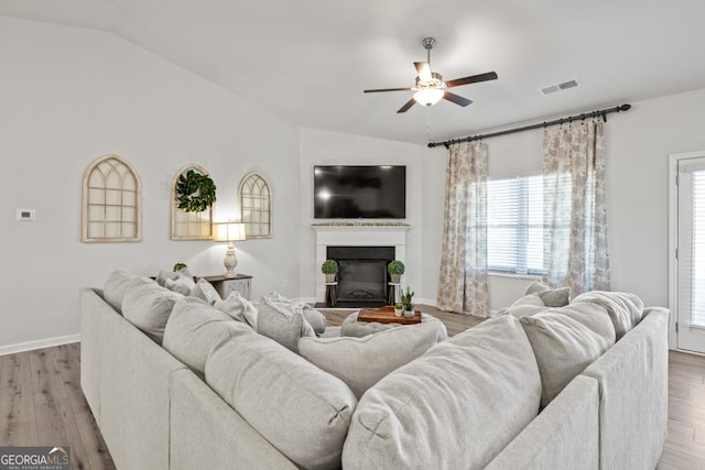 living room with ceiling fan, light wood finished floors, a glass covered fireplace, and lofted ceiling