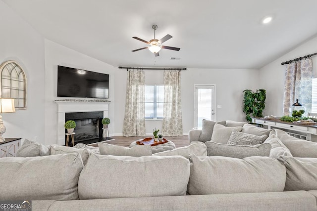 living area with lofted ceiling, ceiling fan, wood finished floors, and a glass covered fireplace