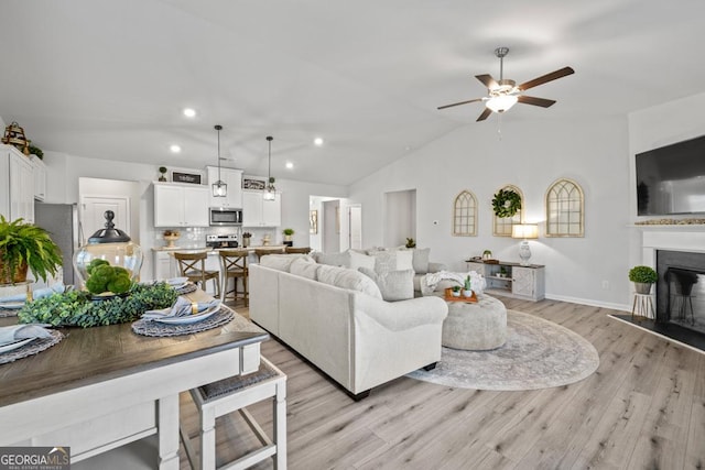 living room with recessed lighting, a glass covered fireplace, vaulted ceiling, ceiling fan, and light wood-type flooring