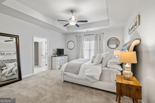 bedroom featuring light carpet, a tray ceiling, connected bathroom, and baseboards