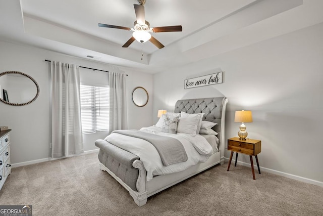 bedroom featuring a tray ceiling, light colored carpet, ceiling fan, and baseboards