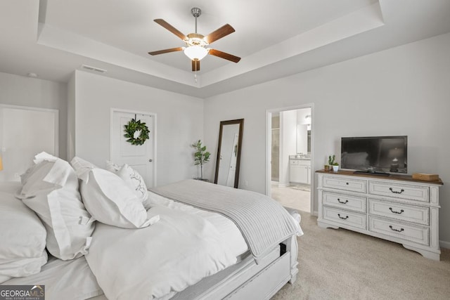 bedroom with a tray ceiling, connected bathroom, light colored carpet, and visible vents