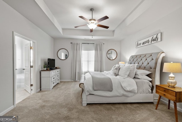 bedroom with light carpet, baseboards, a raised ceiling, ceiling fan, and ensuite bathroom