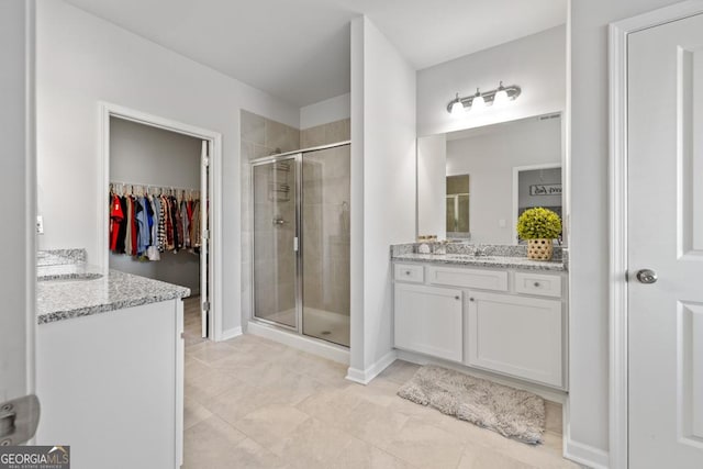 full bathroom with a walk in closet, vanity, baseboards, and a stall shower