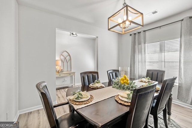 dining room featuring baseboards, light wood finished floors, visible vents, and an inviting chandelier