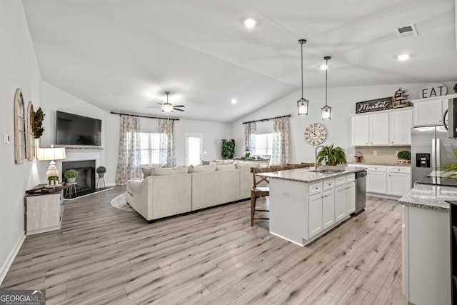 kitchen featuring stainless steel appliances, white cabinets, open floor plan, hanging light fixtures, and a center island with sink