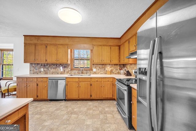 kitchen with stainless steel appliances, a sink, light countertops, and under cabinet range hood