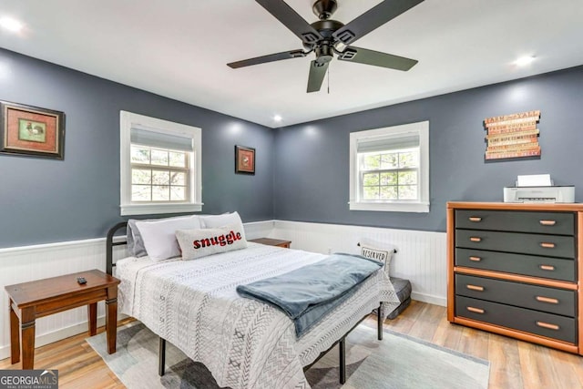 bedroom with light wood-type flooring, a wainscoted wall, and ceiling fan