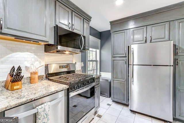 kitchen featuring light tile patterned floors, gray cabinetry, stainless steel appliances, light stone countertops, and tasteful backsplash