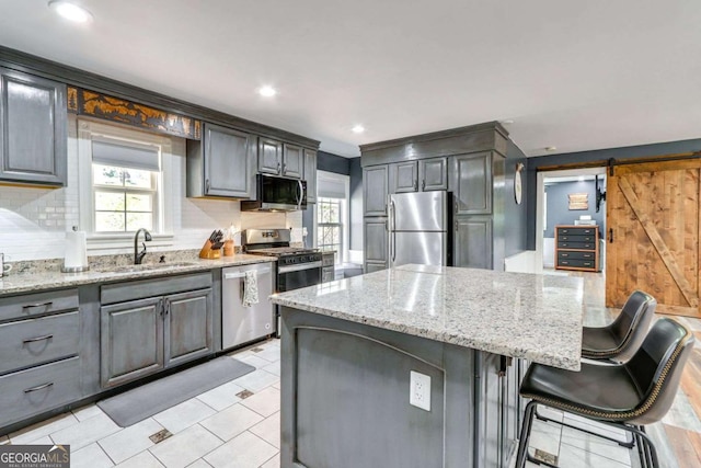 kitchen with a center island, gray cabinetry, a barn door, appliances with stainless steel finishes, and a sink