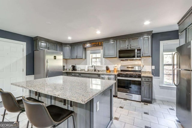 kitchen with light stone counters, stainless steel appliances, a kitchen island, a sink, and tasteful backsplash