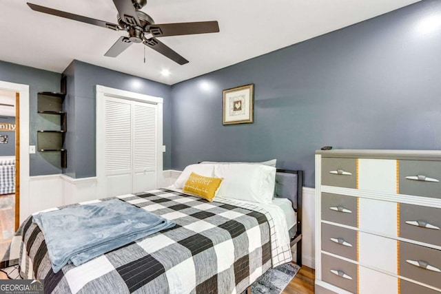 bedroom featuring a wainscoted wall, a ceiling fan, a closet, and wood finished floors