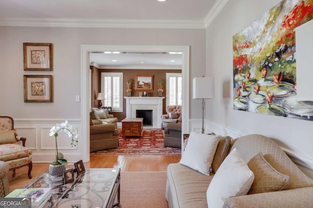 living room featuring a wainscoted wall, light wood-style flooring, a fireplace, and ornamental molding