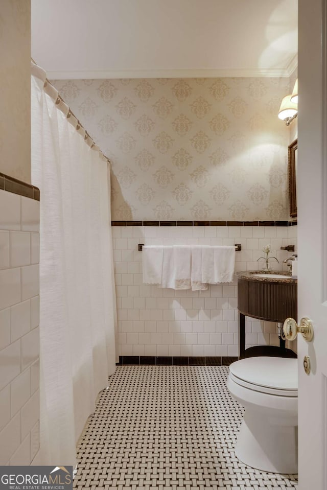 bathroom with a shower with curtain, wainscoting, toilet, and wallpapered walls