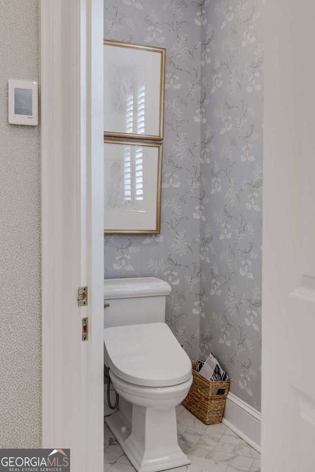 bathroom with toilet, marble finish floor, baseboards, and wallpapered walls