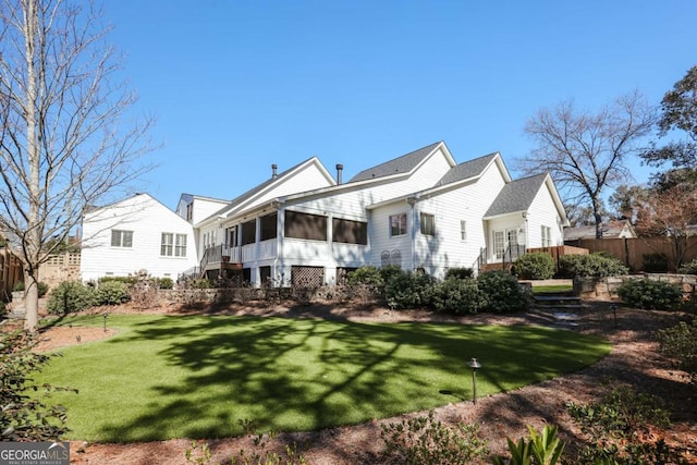 rear view of house featuring a yard, fence, and a sunroom