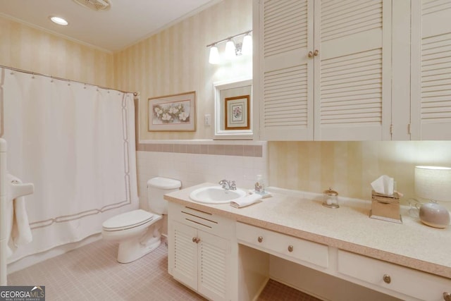 bathroom with tile walls, toilet, wainscoting, vanity, and wallpapered walls