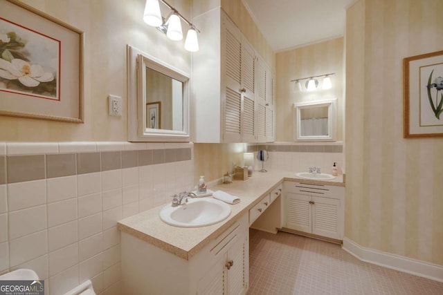 bathroom featuring double vanity, wallpapered walls, tile walls, and a sink