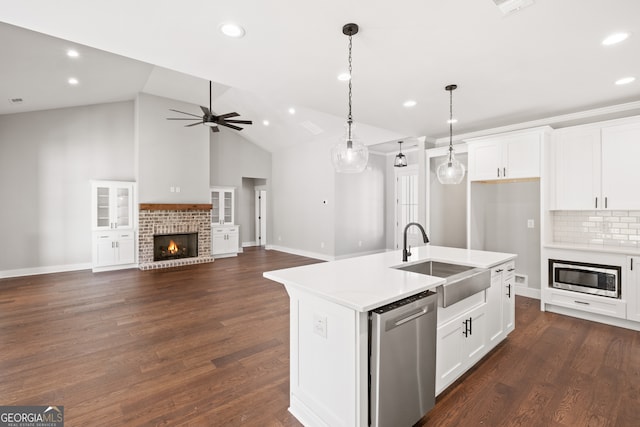 kitchen with a ceiling fan, appliances with stainless steel finishes, dark wood-style flooring, a brick fireplace, and a sink