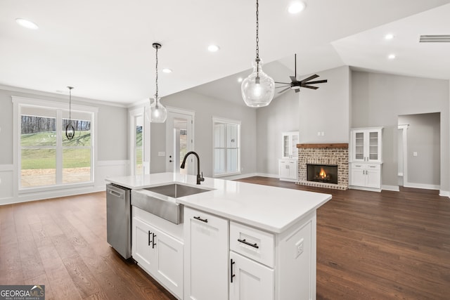 kitchen featuring a kitchen island with sink, a sink, a brick fireplace, dishwasher, and dark wood finished floors