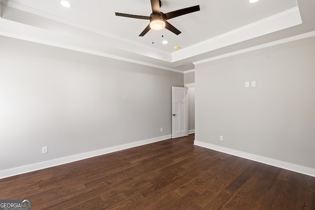 empty room featuring crown molding, a raised ceiling, dark wood finished floors, and baseboards