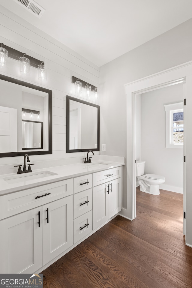 bathroom featuring toilet, wood finished floors, a sink, and visible vents