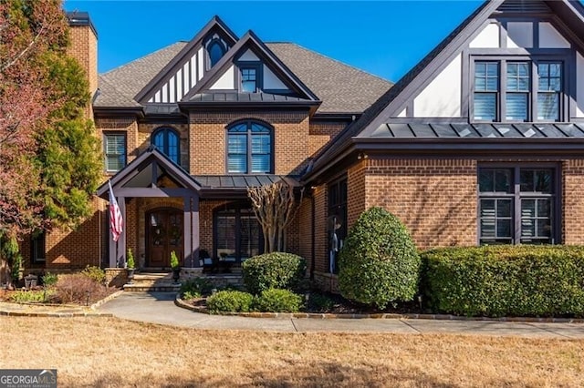 tudor home with metal roof, brick siding, a standing seam roof, and a shingled roof