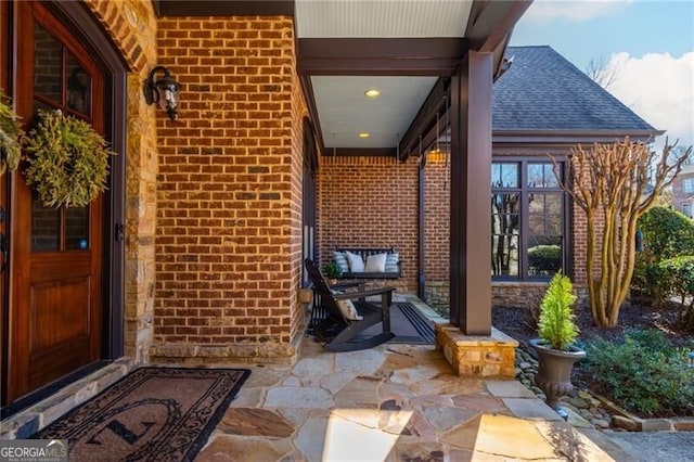 doorway to property featuring brick siding, roof with shingles, and a porch