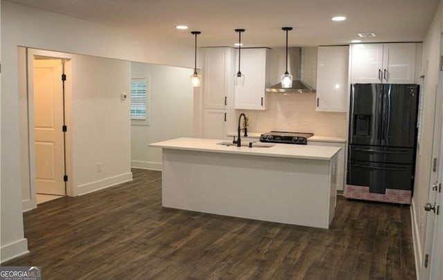 kitchen with pendant lighting, a center island with sink, black fridge with ice dispenser, a sink, and wall chimney range hood