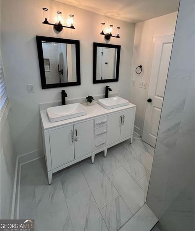 full bathroom featuring marble finish floor, a sink, baseboards, and double vanity