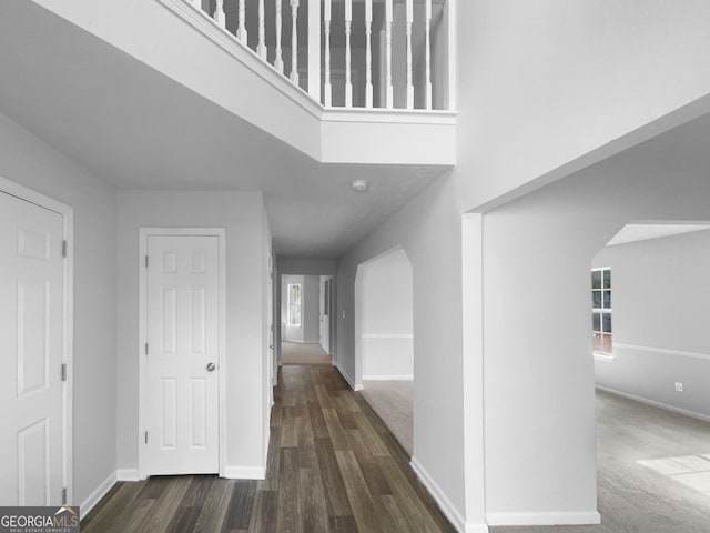 hall with arched walkways, dark wood finished floors, and baseboards