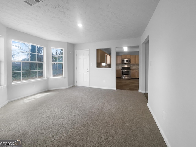 unfurnished living room with a textured ceiling, dark carpet, visible vents, and baseboards