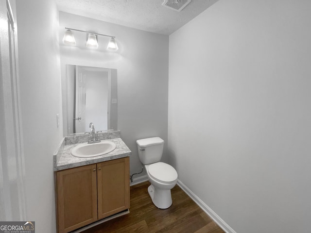 bathroom with a textured ceiling, toilet, wood finished floors, vanity, and visible vents