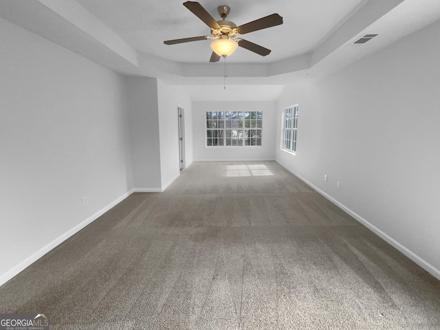 spare room with carpet floors, a ceiling fan, visible vents, baseboards, and a raised ceiling