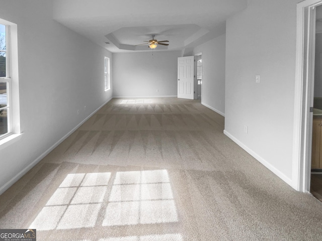 unfurnished living room featuring a raised ceiling, carpet flooring, ceiling fan, and baseboards