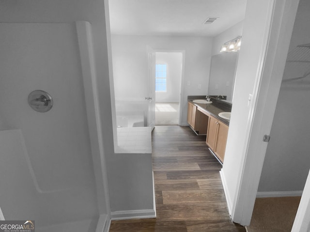 bathroom featuring a tub to relax in, double vanity, visible vents, a sink, and wood finished floors