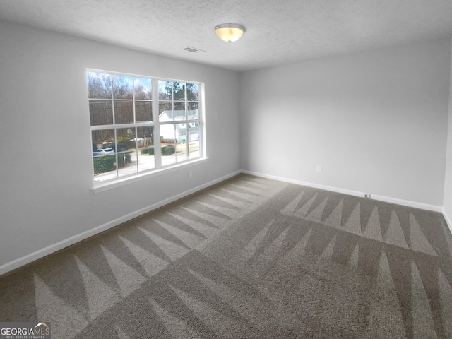 unfurnished room with a textured ceiling, carpet flooring, visible vents, and baseboards