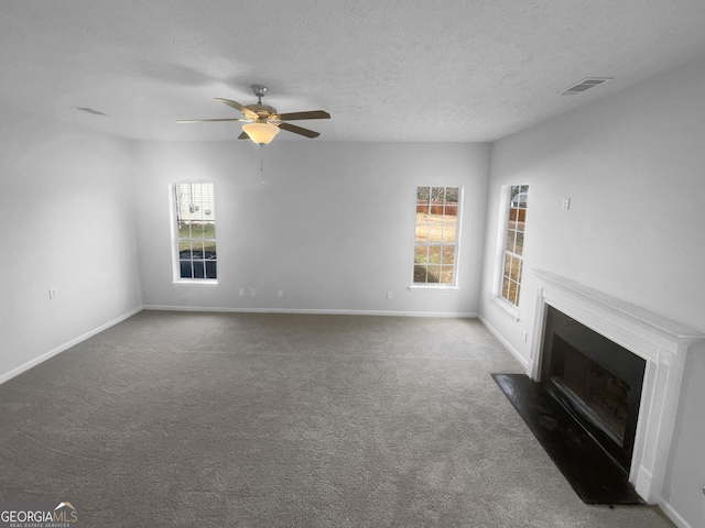 unfurnished living room featuring a textured ceiling, a fireplace with flush hearth, visible vents, baseboards, and dark colored carpet