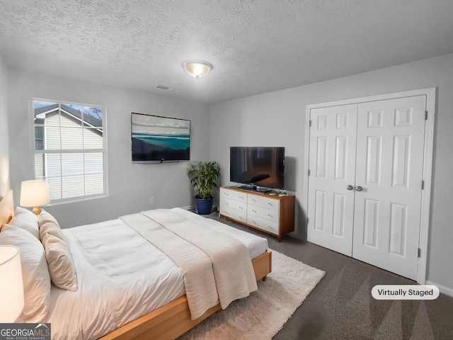 bedroom featuring a textured ceiling, visible vents, dark colored carpet, and a closet