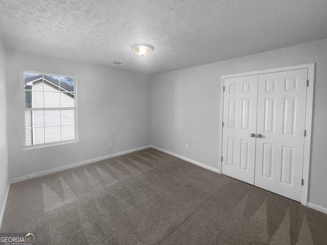 unfurnished bedroom featuring visible vents, baseboards, a textured ceiling, carpet floors, and a closet