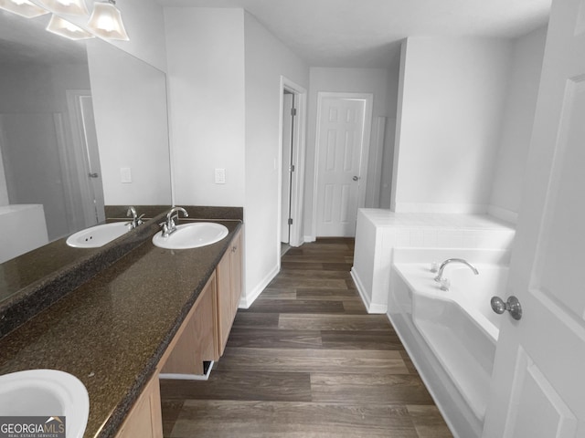 bathroom with double vanity, wood finished floors, a sink, and a bath