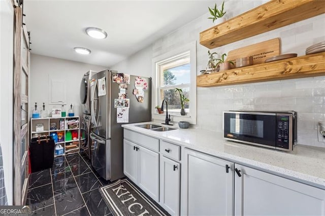 kitchen featuring black microwave, light stone counters, a sink, marble finish floor, and freestanding refrigerator