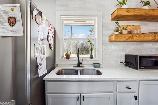 kitchen with black microwave, light stone counters, a sink, freestanding refrigerator, and decorative backsplash