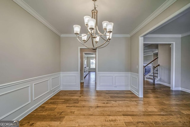 unfurnished dining area with stairway, ornamental molding, wood finished floors, a chandelier, and a decorative wall