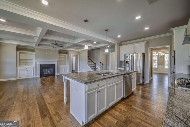 kitchen featuring a center island with sink, appliances with stainless steel finishes, a glass covered fireplace, white cabinetry, and a sink