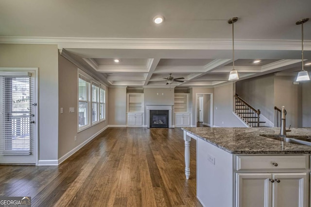 kitchen with a sink, white cabinetry, open floor plan, dark stone counters, and pendant lighting