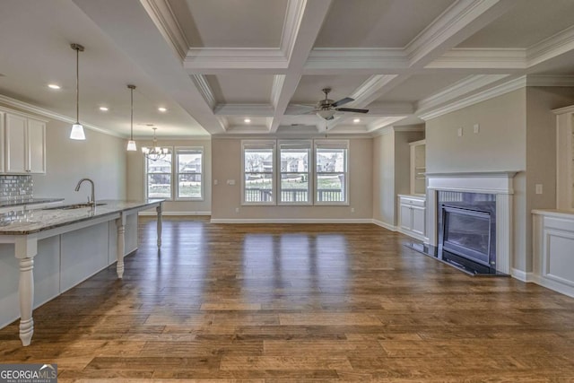 unfurnished living room featuring coffered ceiling, a glass covered fireplace, dark wood-style flooring, a sink, and beam ceiling